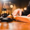 judges gavel on desk with man reading law book in background