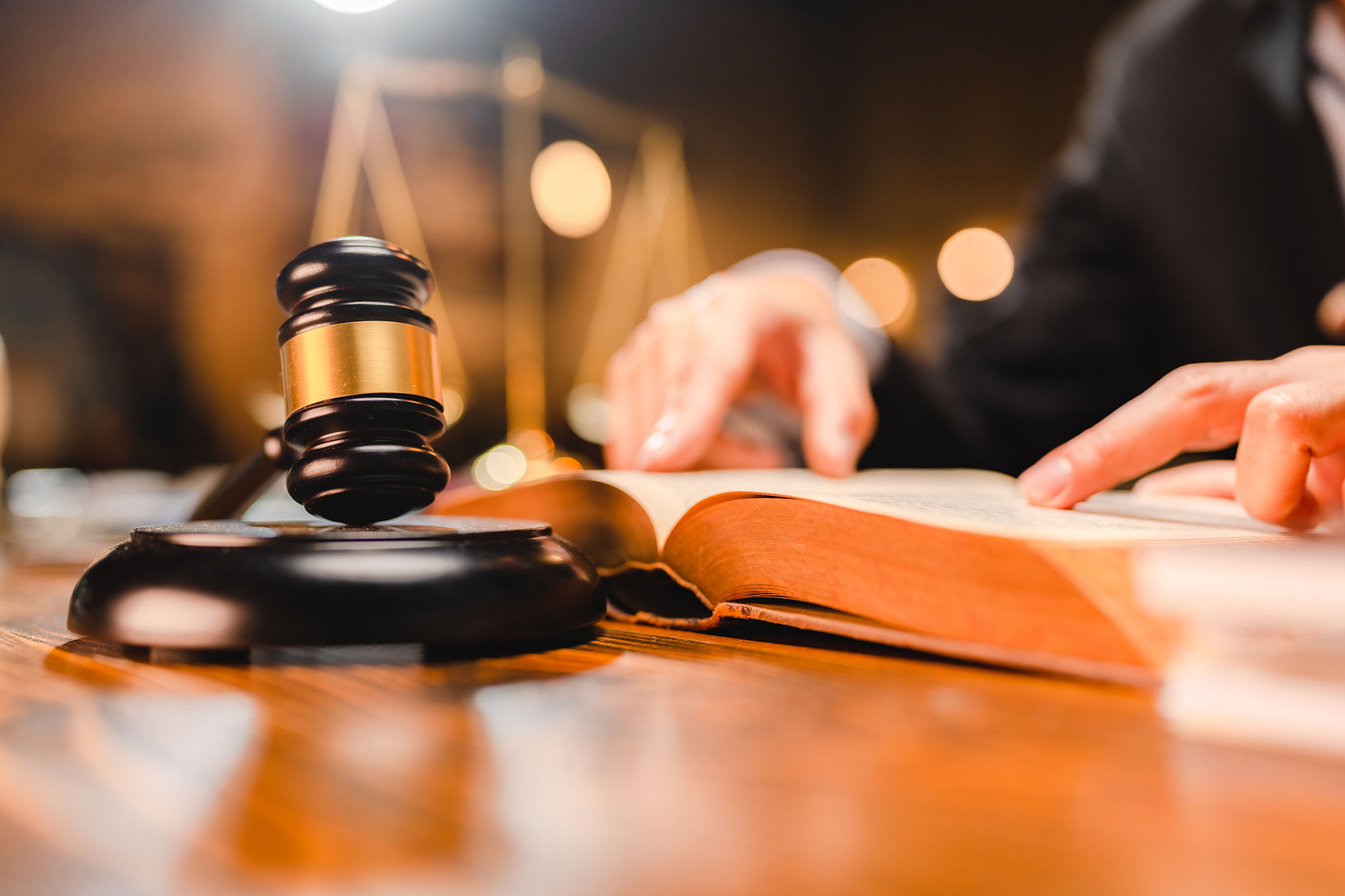 judges gavel on desk with man reading law book in background